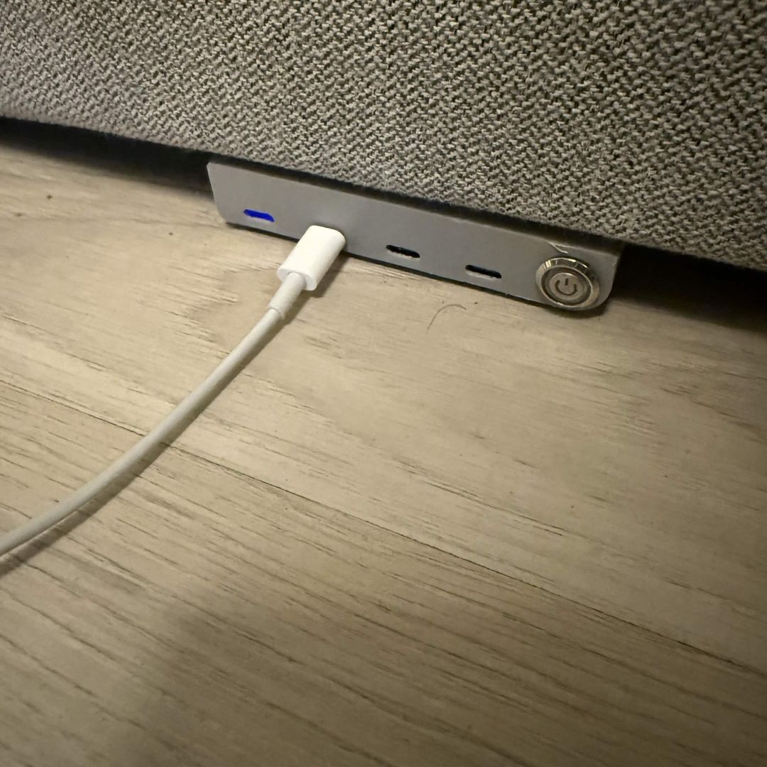 The charging dock built into the edge of a grey couch, switch off, a charging cable plugged into one port.